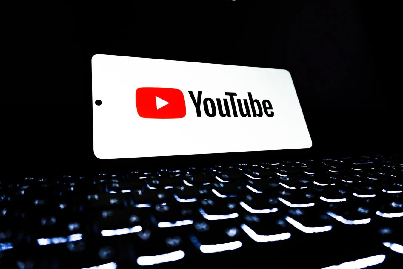 YouTube app icon displayed on a smartphone over an illuminated keyboard, representing digi