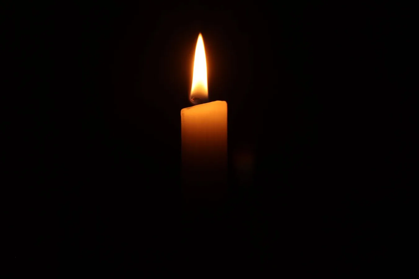 A single burning candle in the dark, casting a warm and serene glow.