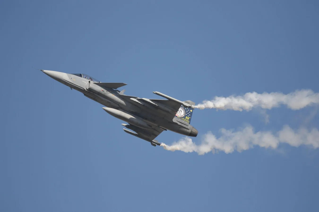 Dramatic shot of a fighter jet soaring with vapor trails against a clear sky.