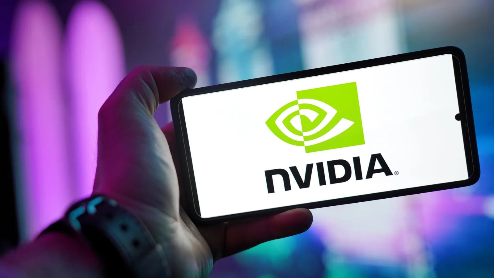 Close-up of a hand holding a smartphone showing the NVIDIA logo on screen with a blurred b
