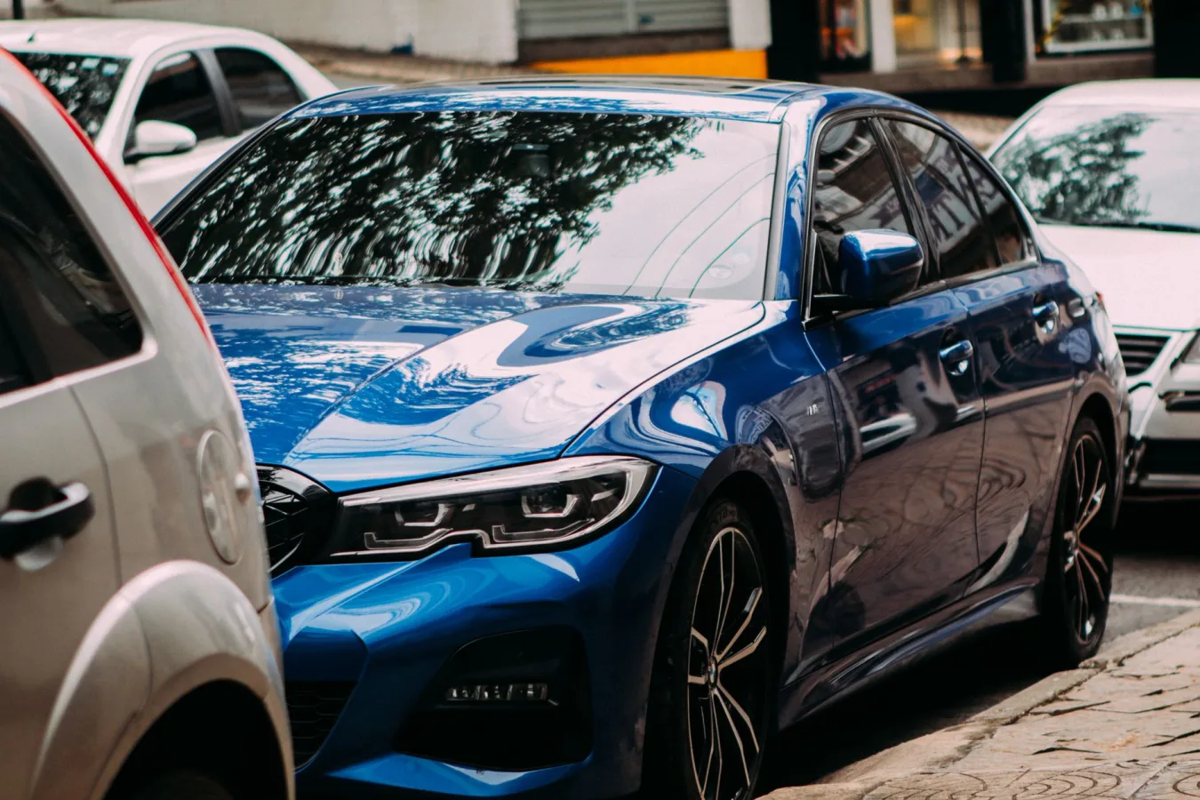 A vibrant blue luxury sedan parked on an urban street among cars.