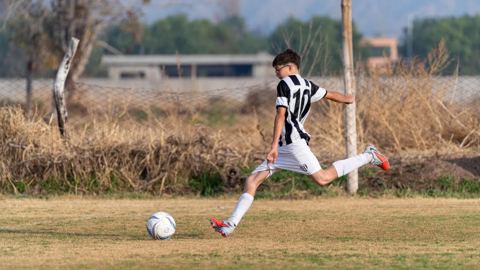 Energetic youth soccer player in striped jersey skillfully kicking the ball on a grassy fi