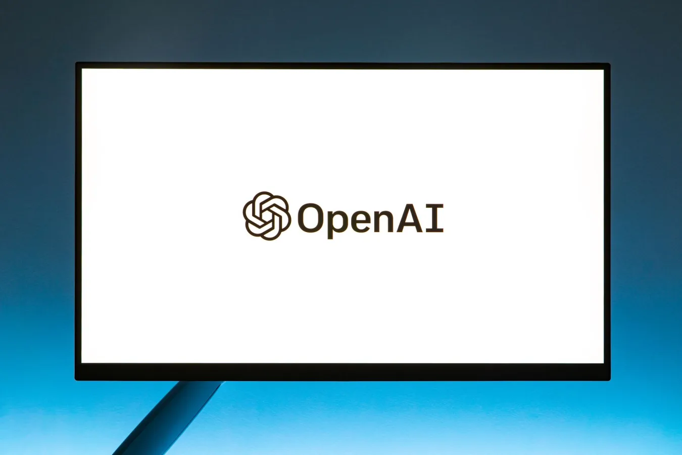 Minimalistic display of OpenAI logo on a monitor with a gradient blue background, represen