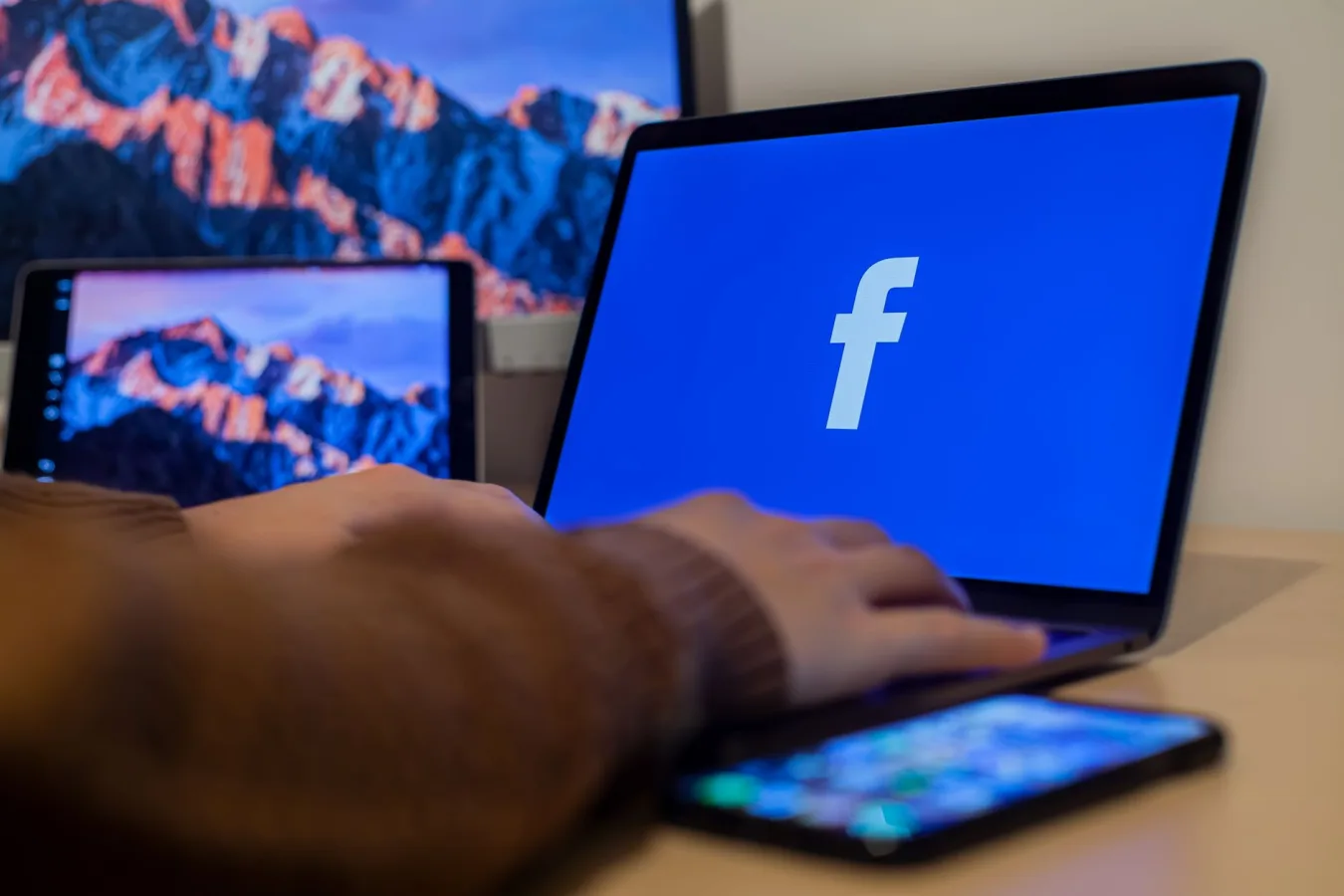 Laptop displaying Facebook at workspace with multiple devices, highlighting modern technol