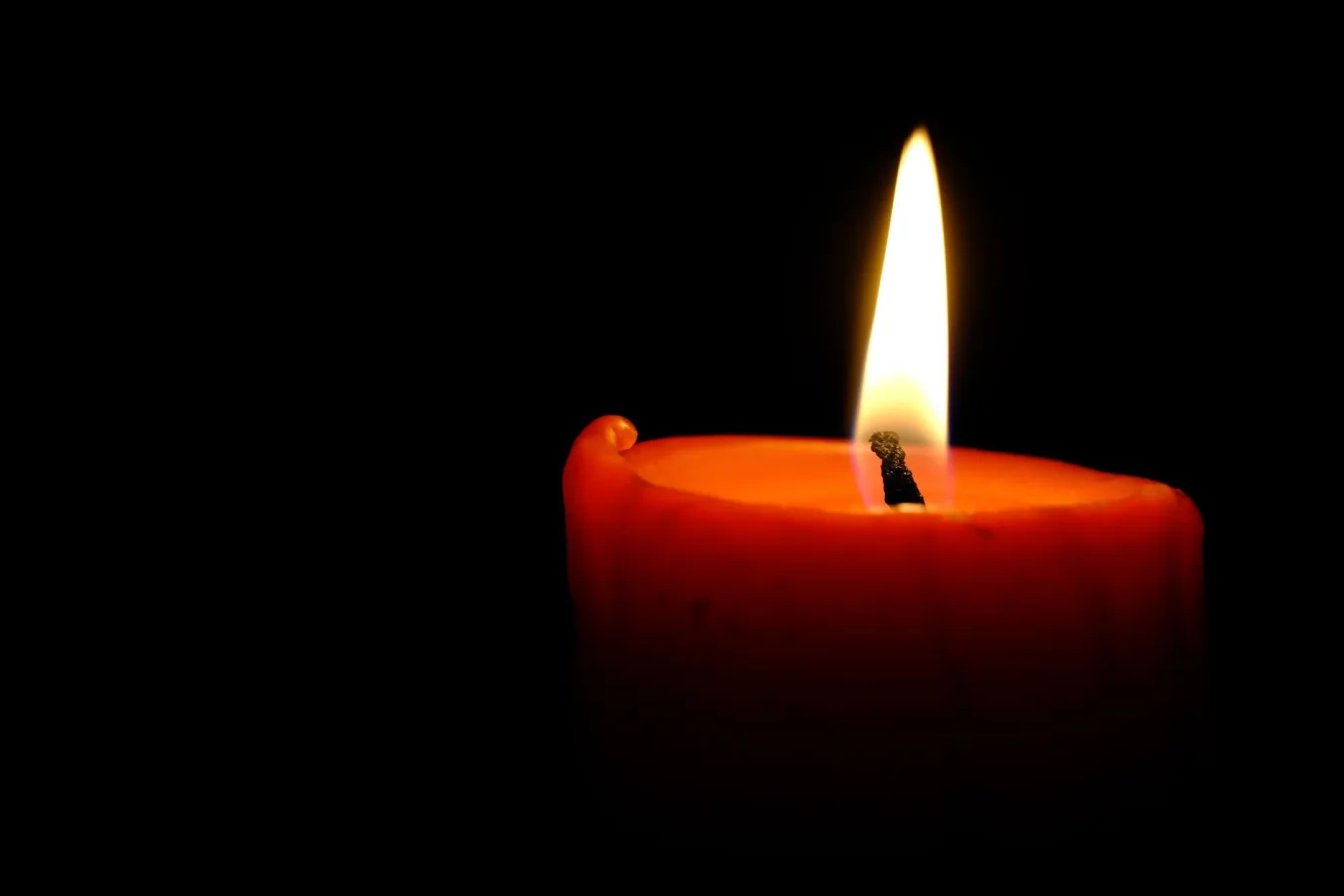 Close-up of a burning candle with a glowing flame against a dark backdrop, creating a warm