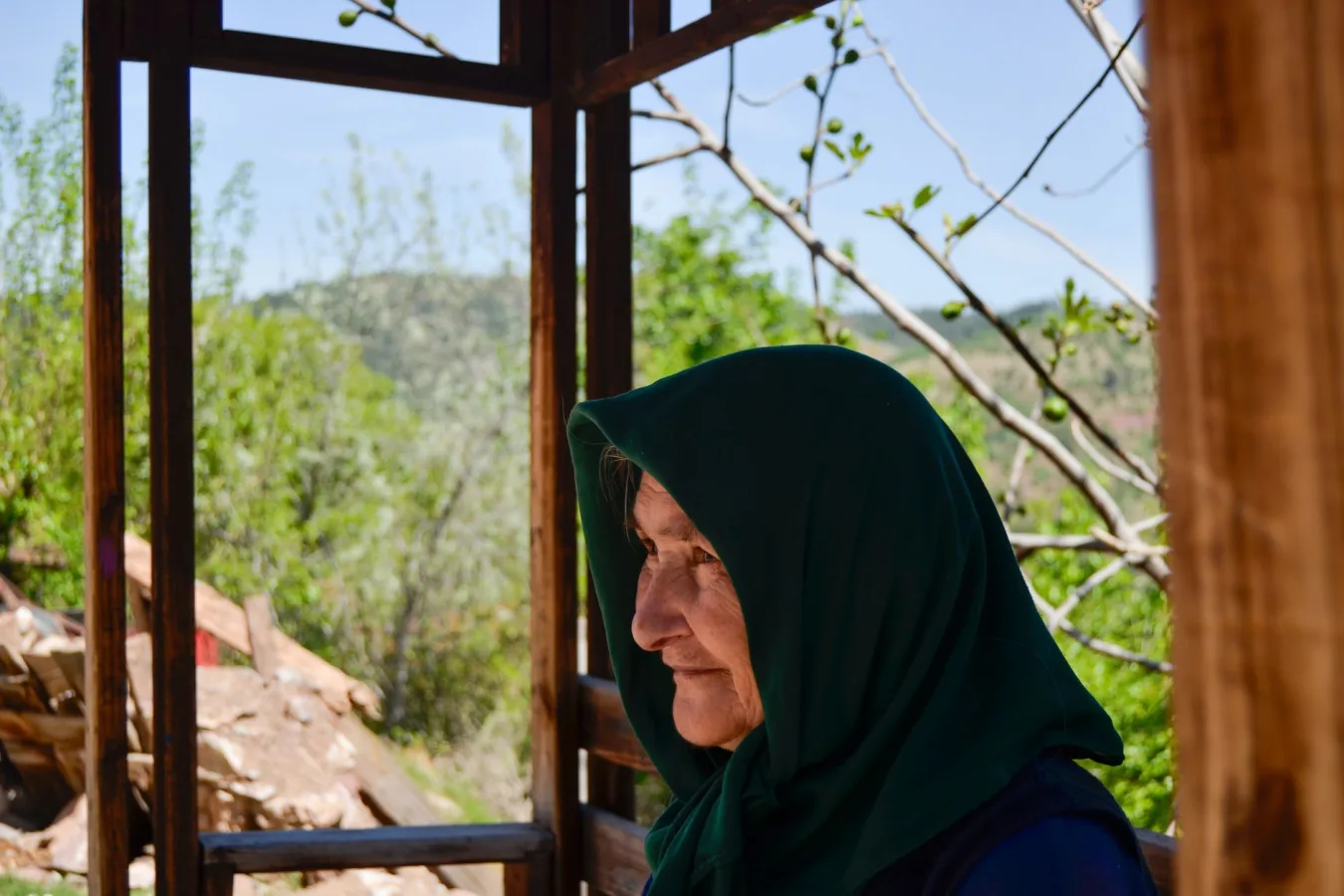 Side profile of a smiling elderly woman in a green headscarf enjoying the outdoors.