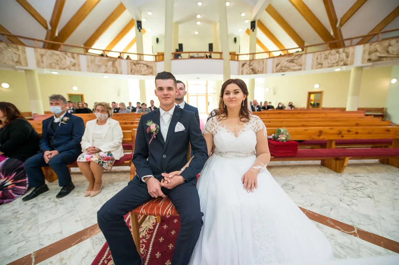A bride and groom seated in a beautifully decorated church, surrounded by guests during th