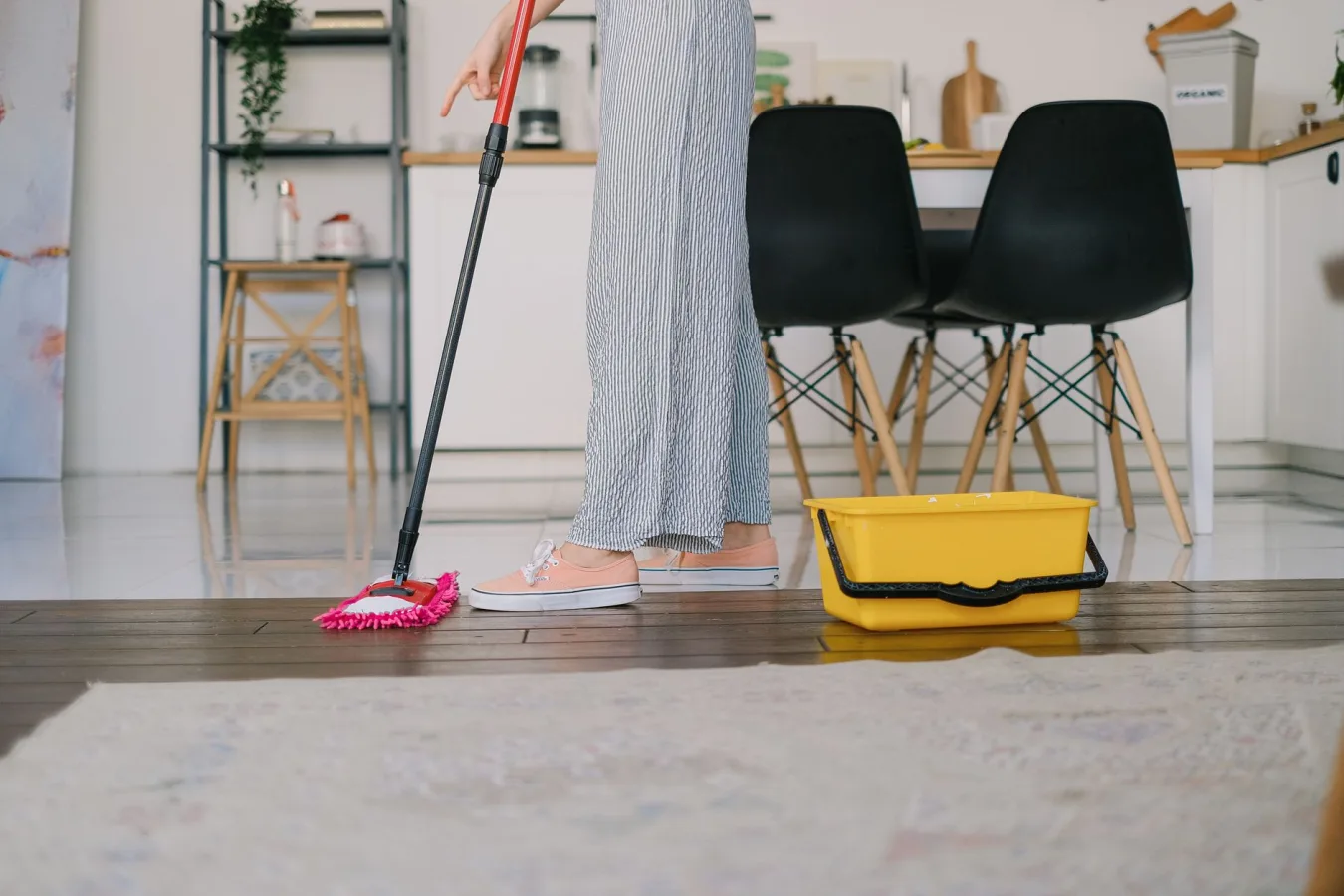 Side view of crop anonymous woman washing parquet with mop against bucket and carpet in ho