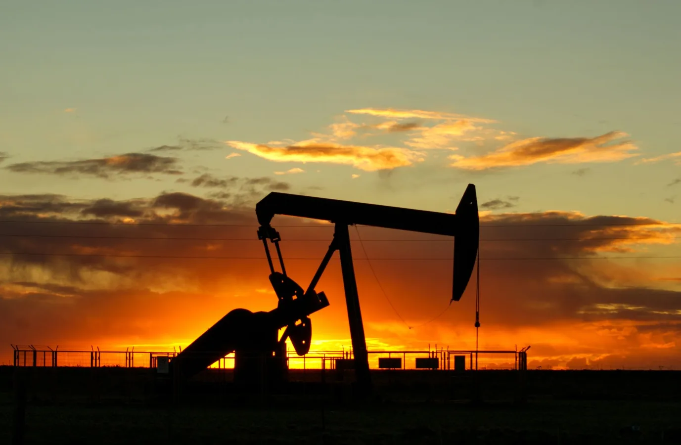 Dramatic silhouette of an oil pump jack against a vibrant sunset sky, emphasizing energy e